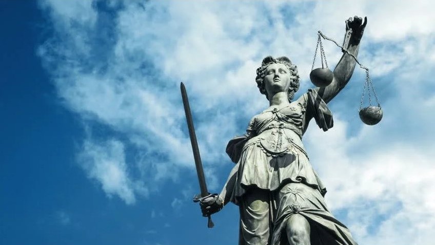 statue of woman holding sword and scales of justice with blue sky and clouds